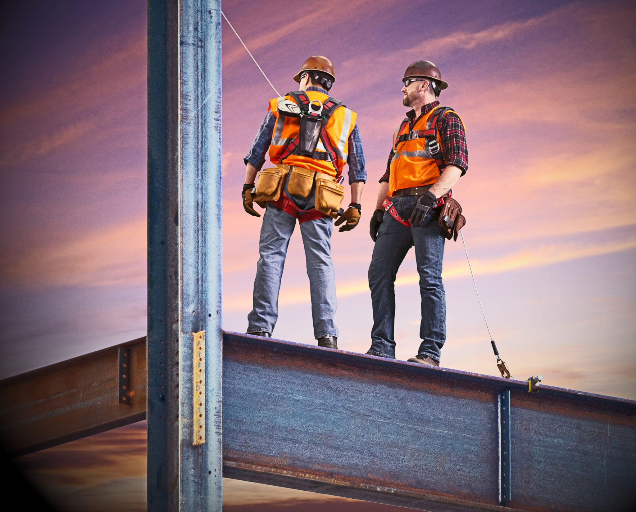 Two construction workers standing on a girder at sunset